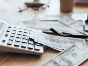 calculator, money, and glasses on cluttered desk