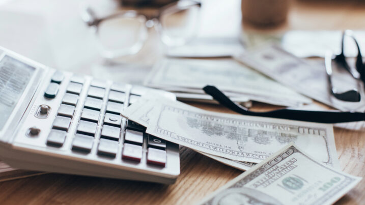 calculator, money, and glasses on cluttered desk